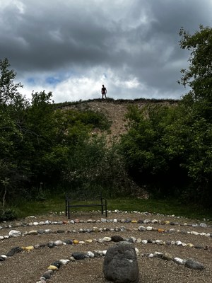 Photo of a participant on a hill behind a medicine wheel on the land. 